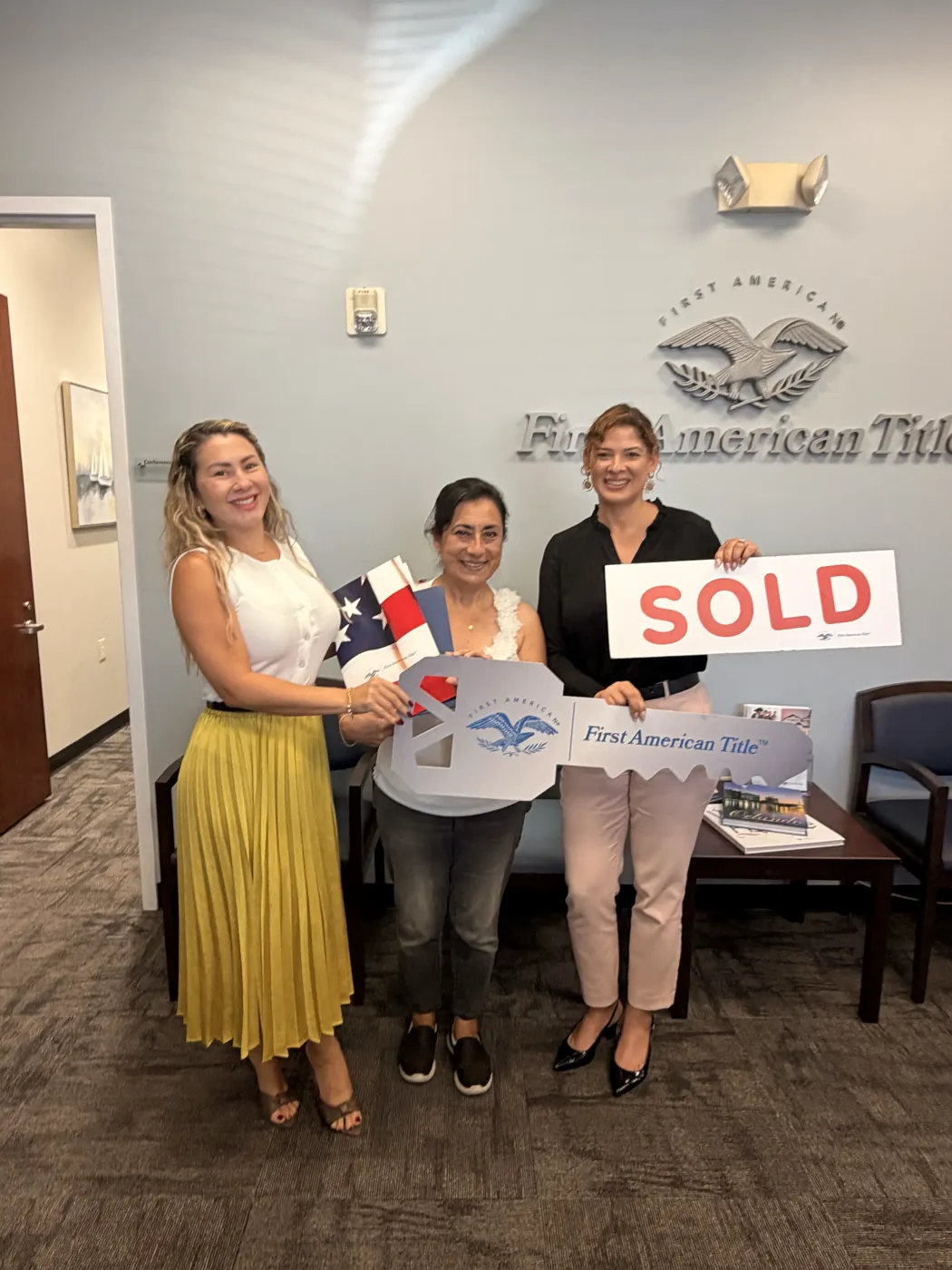 Entrega de llaves a una clienta en las oficinas de First American Title con el cartel de SOLD